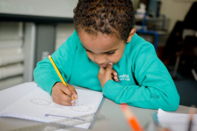 EAL Learners | A picture of a young boy writing at a desk in a school classroom